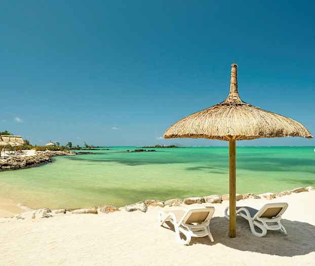 En sandstrand med to liggestole under en parasol lavet af strå, med turkisblåt vand i baggrunden. (AI-genereret tekst)