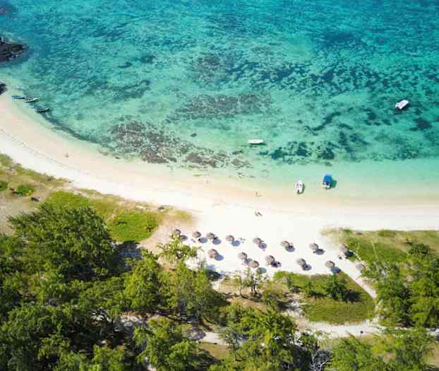 Luftfoto af en tropisk strand med parasoller, både og omkringliggende grønne områder. (AI-genereret tekst)