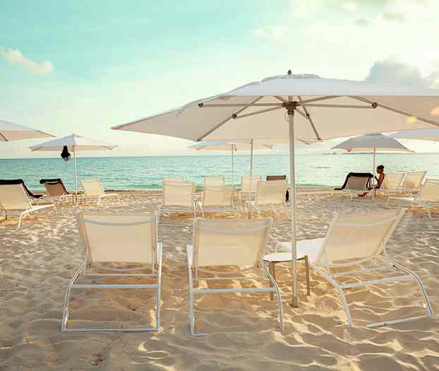 En sandstrand med liggestole og parasoller. Havet er synligt i baggrunden under en klar himmel. (AI-genereret tekst)