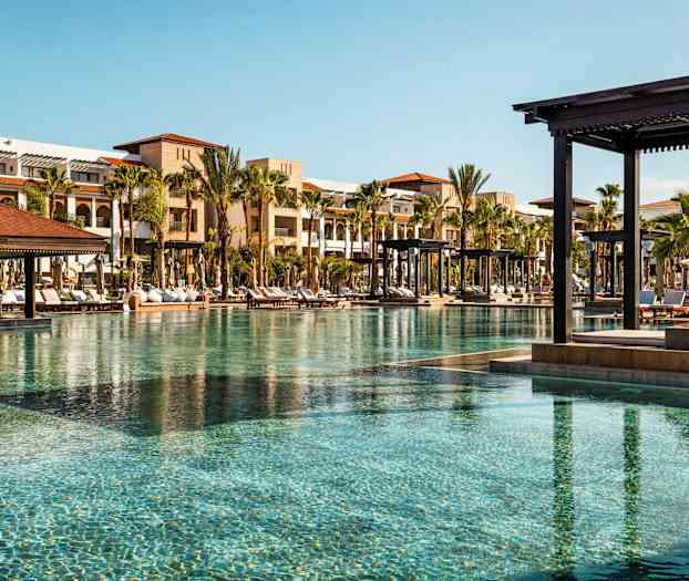 Poolområde med liggestole og bygninger i baggrunden. (AI-genereret tekst)