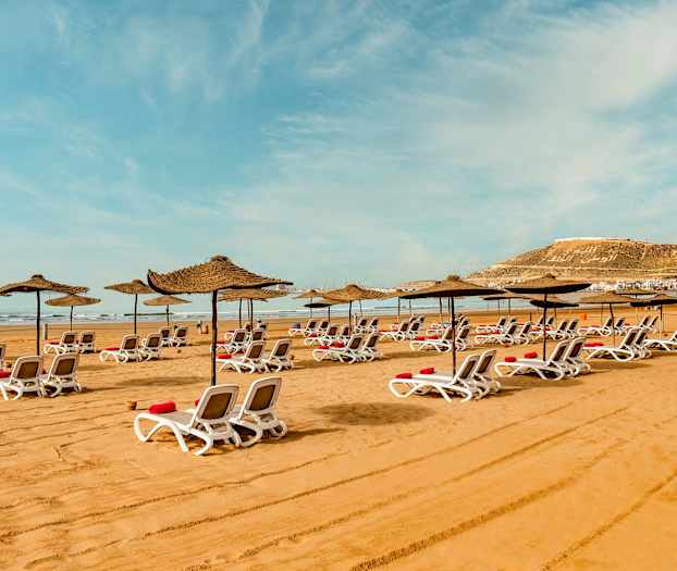 Liggestole med parasoller på sandstrand. (AI-genereret tekst)