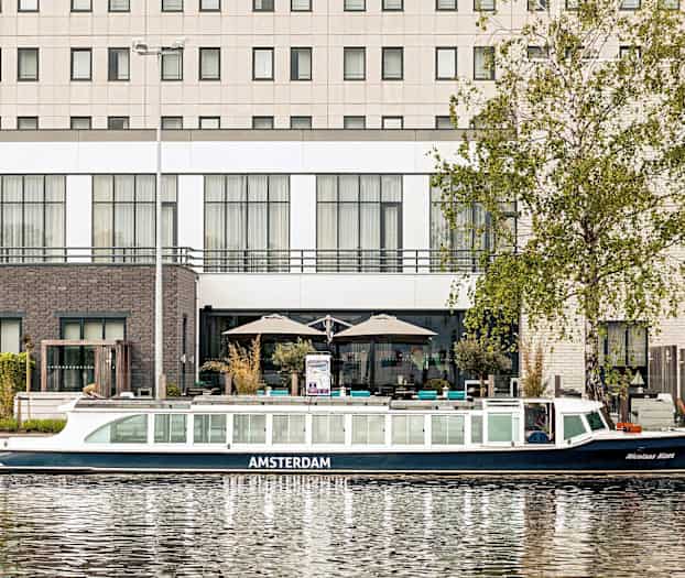 Billede af en kanalbåd foran en bygning ved vandet. (AI-genereret tekst)