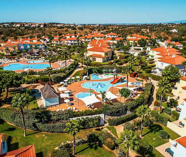 Luftfoto af et feriekompleks med pools og farverige huse. (AI-genereret tekst)