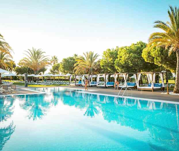 En udendørs pool omgivet af liggestole og palmer. (AI-genereret tekst)