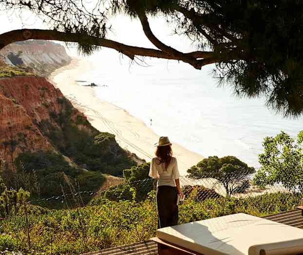 Kvinden står ved kanten med udsigt over en sandstrand og klippeformationer. (AI-genereret tekst)