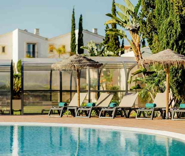 Solsenge og parasoller ved en pool med bygninger og vegetation i baggrunden. (AI-genereret tekst)