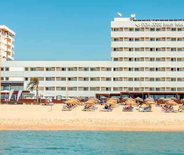 Hotel ved stranden med parasoller og liggestole. (AI-genereret tekst)