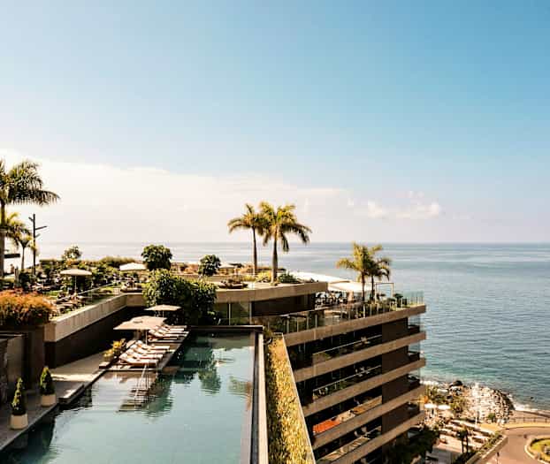 En udsigt over et hotelområde ved havet med swimmingpools og palmer. (AI-genereret tekst)