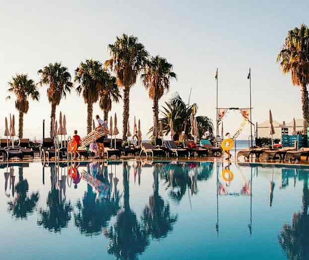 Poolområde med liggestole, parasoller og palmer i baggrunden. (AI-genereret tekst)