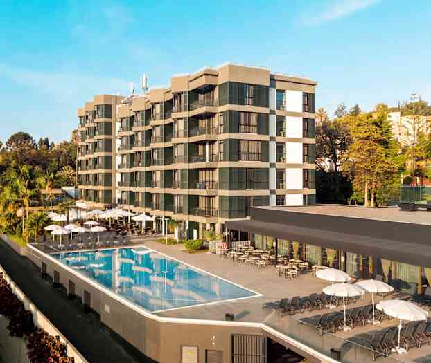 Billede af et hotel med udendørs pool og liggestole, omgivet af træer og vegetation. (AI-genereret tekst)