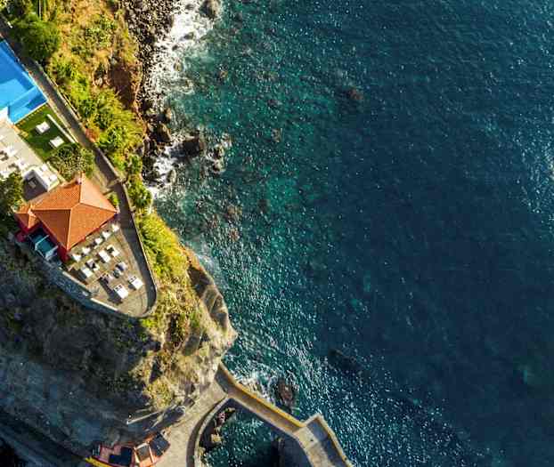 Dronebillede af en klippe med en bygning og pool tæt på havet. (AI-genereret tekst)