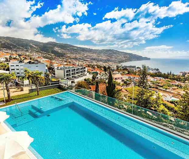 Udsigt over en pool med omkringliggende bygninger og havet i baggrunden. (AI-genereret tekst)