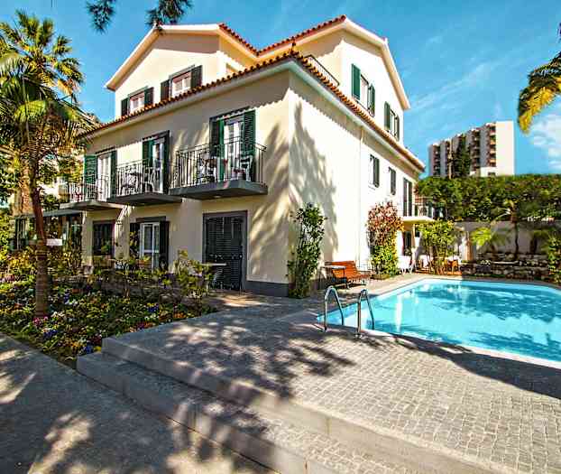 En bygning omgivet af træer med en pool i forgrunden. (AI-genereret tekst)