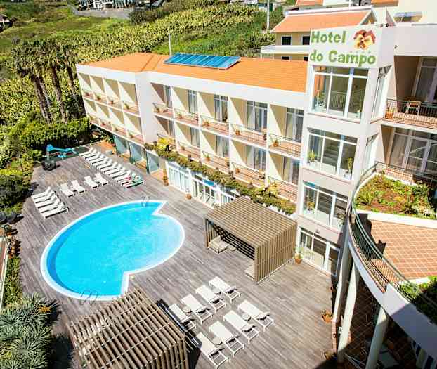 Hotellet har en udendørs pool og liggestole på en terrasse. Bygningen har flere etager og orange tage. (AI-genereret tekst)