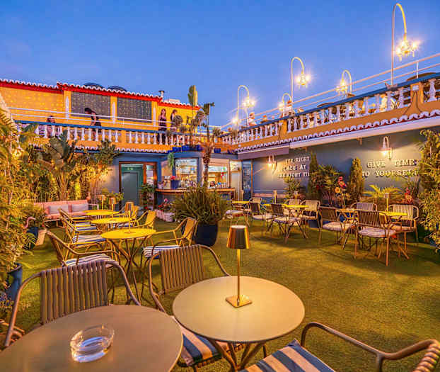 En udendørsterrasse med borde og stole, dekoreret med planter og lyskilder. (AI-genereret tekst)