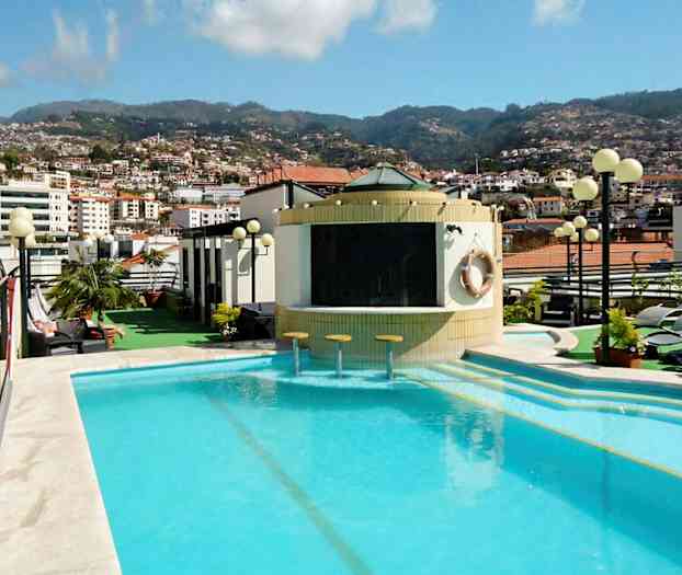 En udendørs pool på et hotel med udsigt over byen og bjergene i baggrunden. (AI-genereret tekst)