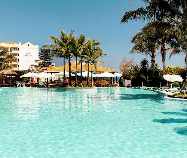 En udendørs pool med palmer og liggestole omkring. (AI-genereret tekst)