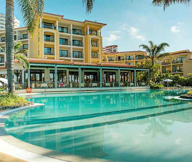 Hotelfacade ved en stor pool omgivet af palmer. (AI-genereret tekst)