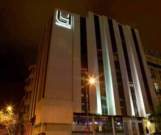 Et hotel med moderne ydre fotograferet om natten. Bygningens facade er oplyst. (AI-genereret tekst)