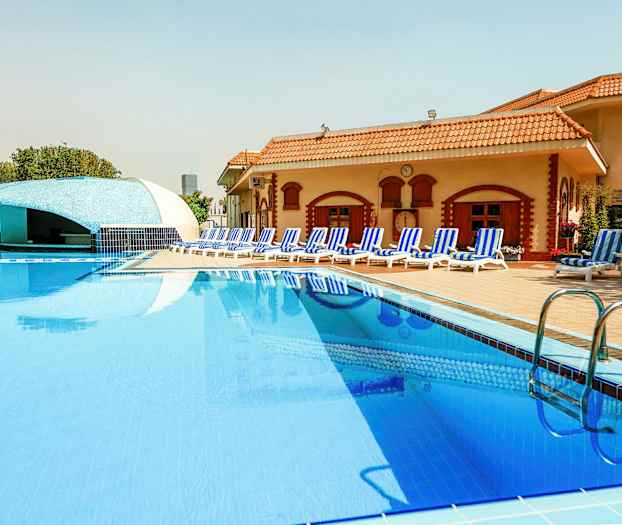 En pool ved et hotel med liggestole og en bar i baggrunden. (AI-genereret tekst)