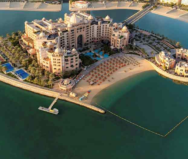 Luftfoto af et luksuriøst hotelkompleks ved en strand med liggestole og parasoller, omgivet af vand. (AI-genereret tekst)