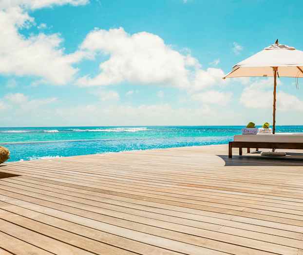 Liggestole og parasol på et trædæk ved havet. (AI-genereret tekst)