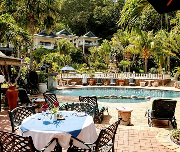 En udendørs pool omgivet af palmer og grønt med en møbleret siddegruppe nær vandet. (AI-genereret tekst)