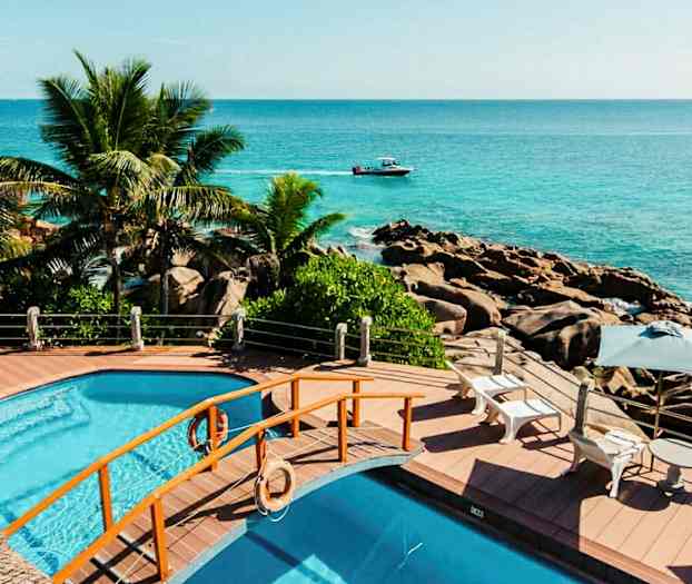 Poolområde med udsigt over havet, omgivet af palmer og klipper. (AI-genereret tekst)