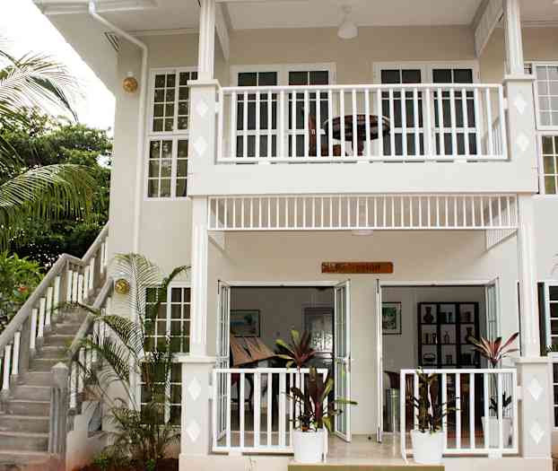 Indgangen til en toetagers bygning med et skilt ved indgangen, hvor der står "Reception", og en omkringliggende have. (AI-genereret tekst)