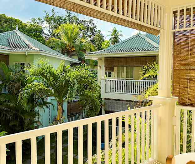 En udsigt fra en altan, der viser et frodigt område med pastelfarvede huse og palmer. (AI-genereret tekst)