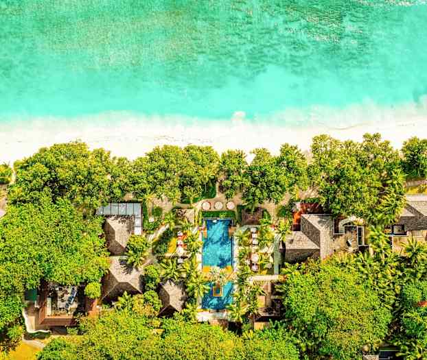 Luftfoto af et hotel ved en strand med pool, omgivet af frodig vegetation. (AI-genereret tekst)