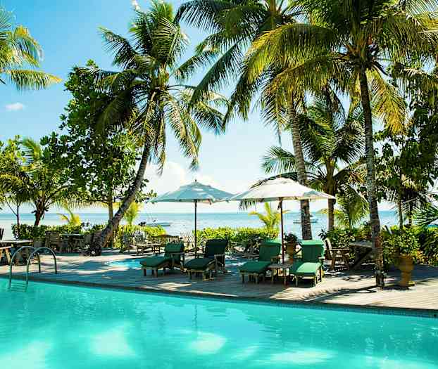 Et billede af en pool omgivet af liggestole med parasoller, omgivet af palmer og grønt med udsigt over havet. (AI-genereret tekst)