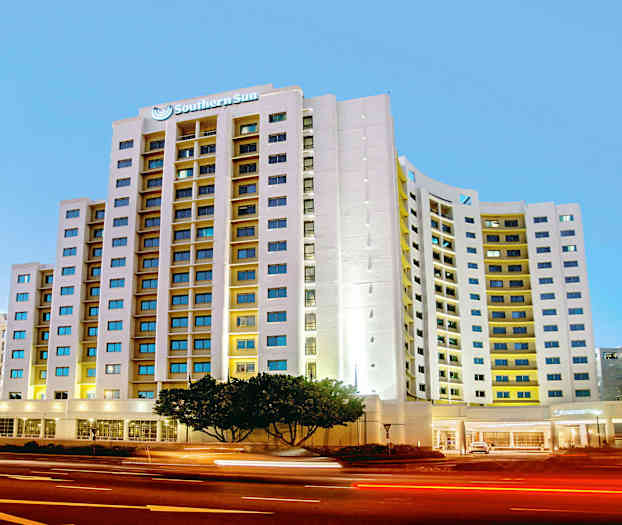 Et moderne hotel med en høj bygning og mange vinduer ligger ved en trafikeret vej om aftenen. (AI-genereret tekst)