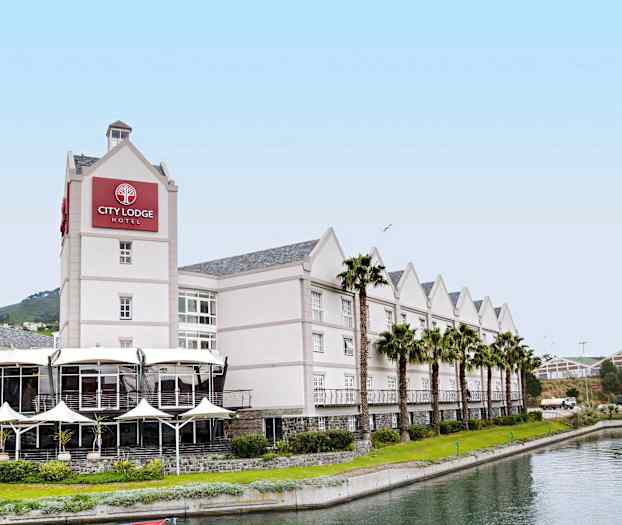 Et hotel med lys facade, kantet af palmer og en kanal foran. (AI-genereret tekst)