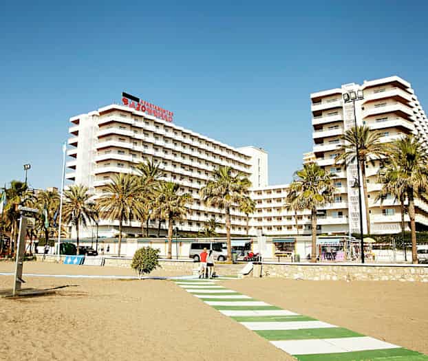 En strandpromenade foran høje lejlighedsbygninger med palmetræer i forgrunden. (AI-genereret tekst)