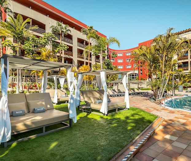 Billede af en pool med liggestole og omkringliggende beplantning ved et hotel. (AI-genereret tekst)