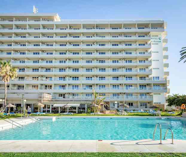 Et lejlighedshotel med altaner foran en swimmingpool og omkringliggende have. (AI-genereret tekst)