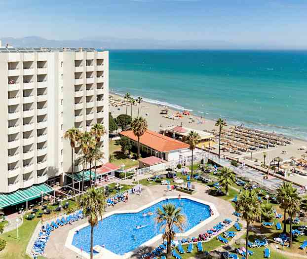 Et hotel med swimmingpool og liggestole tæt på en sandstrand ved havet. (AI-genereret tekst)