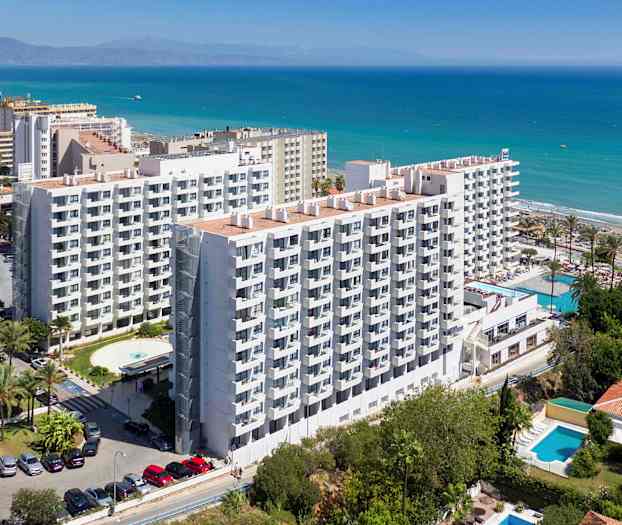 Billede af et fleretagers hotel ved kysten med havet synligt i baggrunden. (AI-genereret tekst)