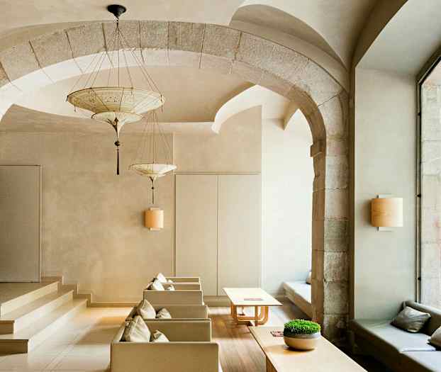 Et elegant indrettet rum med hvælvede buer, moderne møbler og store vinduer ud mod en gade. (AI-genereret tekst)