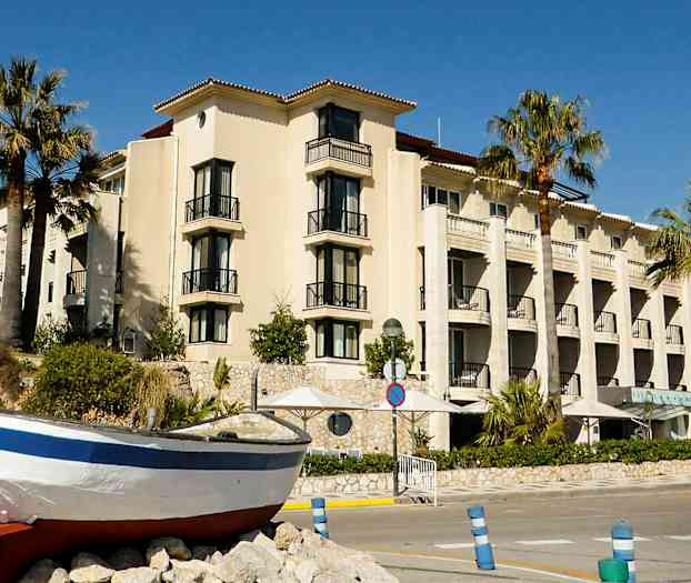 En bygning med altaner og palmer foran samt en båd på land. (AI-genereret tekst)