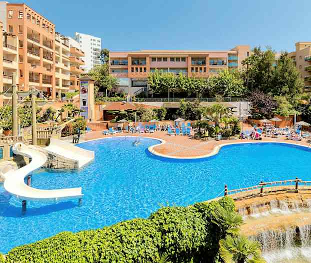 Stort poolområde med vandrutsjebane og omkringliggende hotelbygninger. (AI-genereret tekst)