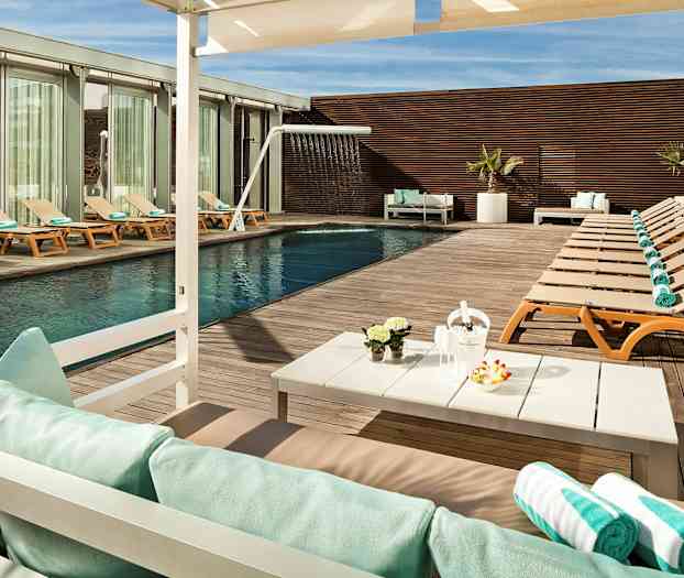 En udendørs swimmingpool med liggestole og håndklæder på et trægulv, samt et bord med dekorationer og parasol. (AI-genereret tekst)