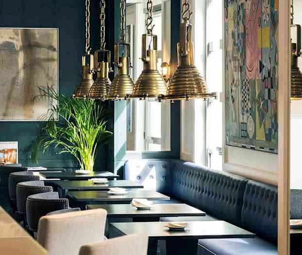 Interiør af en restaurant med mørkeblå vægge, kunstværker, hængende lamper og siddepladser ved borde. (AI-genereret tekst)