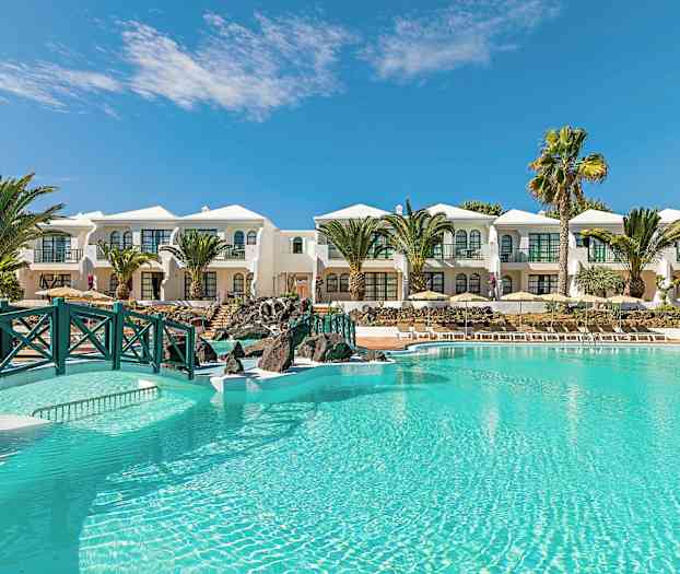 En lyseblå pool foran hvide bygninger med palmer og klar himmel i baggrunden. (AI-genereret tekst)