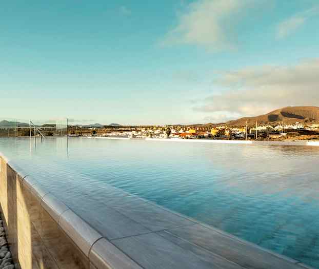 En infinitypool under en klar himmel med udsigt over en by og bjerge i baggrunden. (AI-genereret tekst)