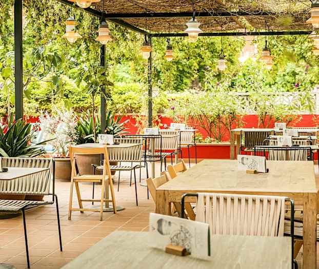 En udendørs servering med borde og stole, omgivet af grønt og røde vægge. (AI-genereret tekst)