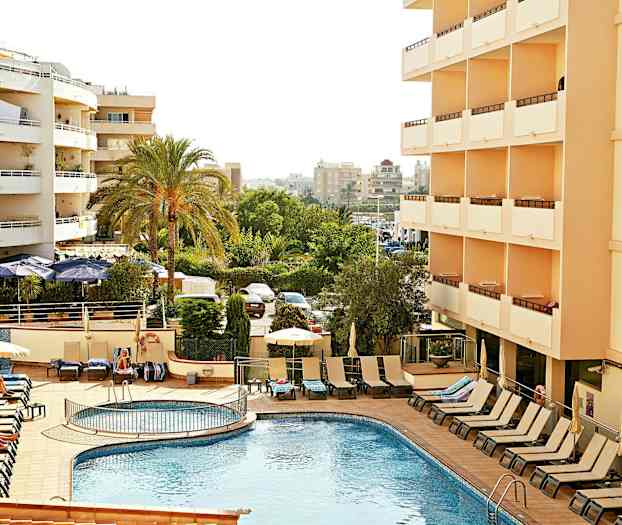 Hotel med udendørs pool og liggestole, omgivet af grønne træer og højhuse. (AI-genereret tekst)