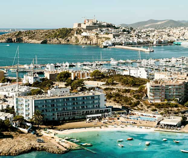 En kystby med flere bygninger og en småbådehavn; små både og en strand ses i forgrunden. (AI-genereret tekst)