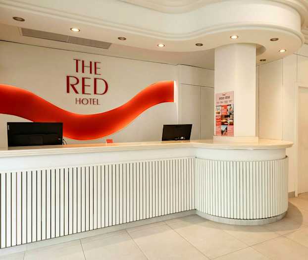 Hotelreception med hvidt interiør og rødt logo på væggen. (AI-genereret tekst)